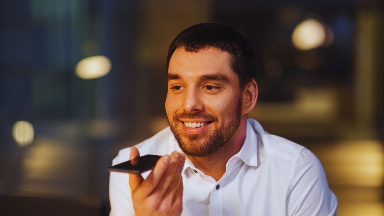 A blind man smiling while holding his phone in front of him, sitting looking relaxed and engaged in conversation