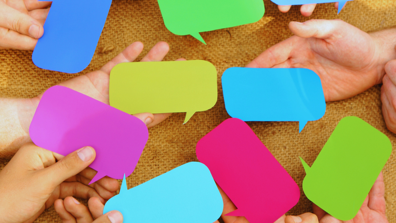Multiple hands holding colorful speech bubbles together, representing group conversation and connection