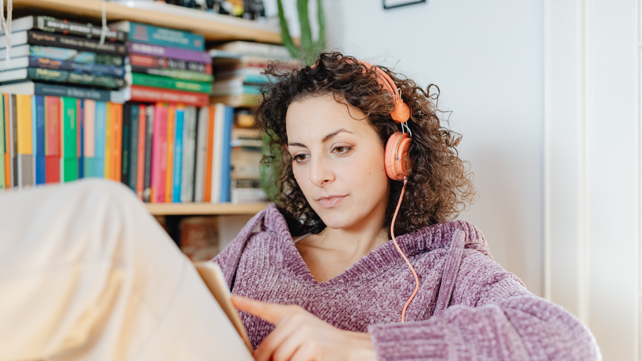 Woman relaxing at home wearing headphones, listening to audio content on her phone