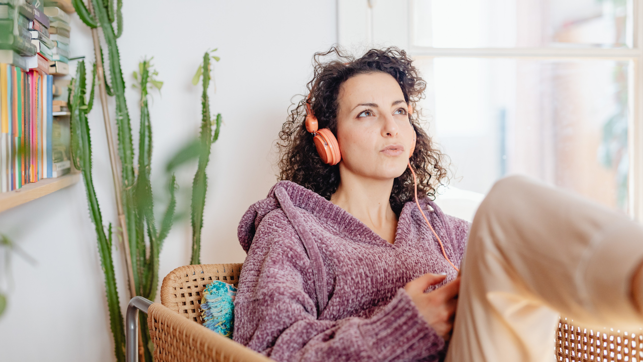 Woman relaxing at home wearing headphones, listening to audio content on her phone