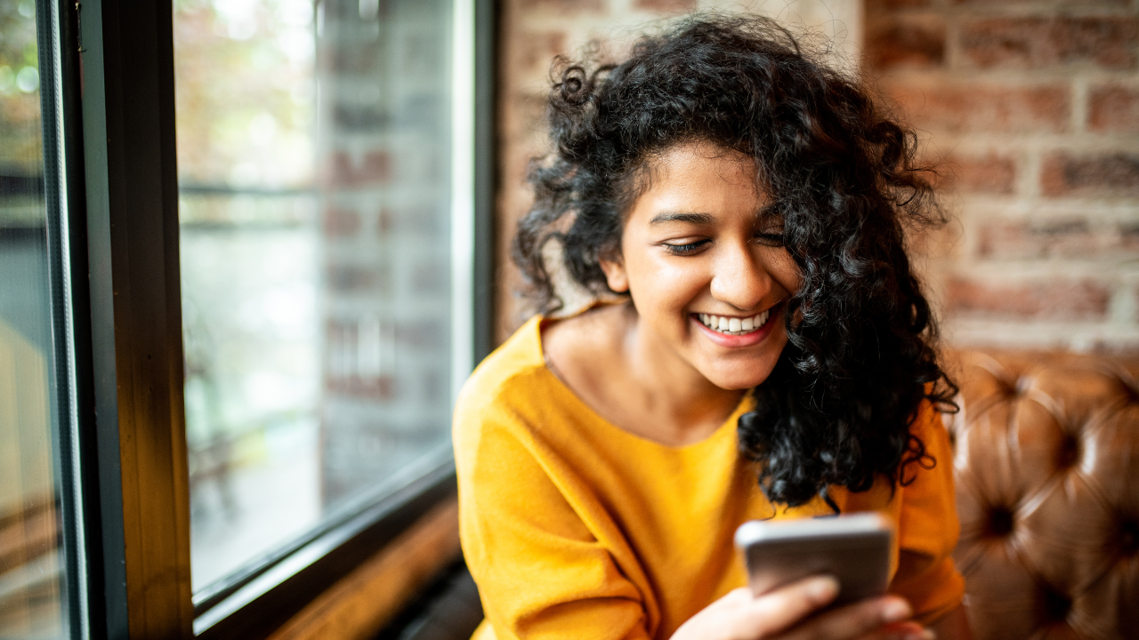 Person in comfortable setting looking thoughtfully at phone, suggesting personal development